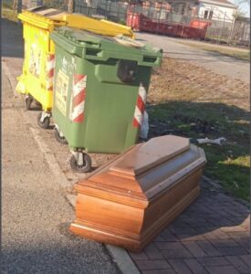 Una bara vuota accanto ai rifiuti